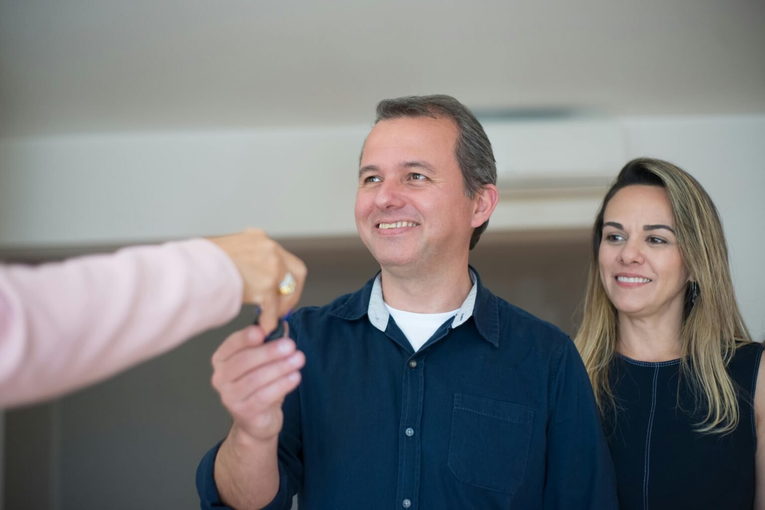 Smiling couple receiving keys, celebrating new home purchase indoors.
